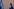 Die Richterin Tomoko Akane geht in einer blauen Robe an einer Wand entlang, links in der Ecke die blaue Flagge des Internationalen Strafgerichtshofs