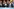 Freude in München - Markus Söder und Dominik Krause geben sich die Hand und sind fröhlich, umgeben von Menschen, die hellblaue Schals mit der Aufschrift: München 20xx tragen