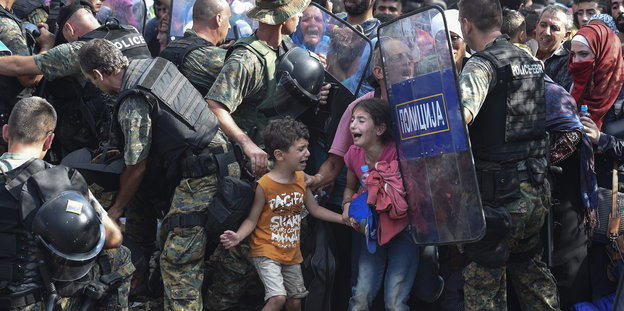 Zwei Kinder umringt von Menschen und Soldaten, sie weinen