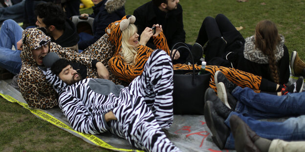 Menschen in Tierkostümen liegen auf einer Wiese in Paris