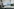 Ein Schreibtisch mit Computer und Tastatur, auf dem Bildschirm sind erkennungsdienstliche Bilder von Händen zu sehen, auf dem Tisch ein Gerät, um Fingerabdrücke abzunehmen, und eine Kamera mit Stativ steht daneben