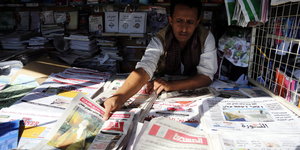 Ein Zeitungsverkäufer in einem Kiosk bietet seine Zeitungen zum Verkauf an.