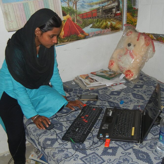 Eine Frau sitzt mit Laptop auf einem Bett