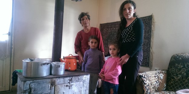 Eine alte Frau, eine junge Frau und zwei Mädchen stehen neben einem alten Herd in der Küche