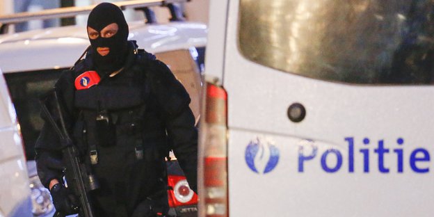 Ein vermummter Polizist läuft neben einem Polizei-Fahrzeug mit der Aufschrift „Politie“.