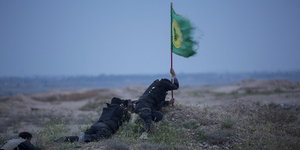 drei Kämpfer mit einer schiitischen Fahne liegen in der Nähe von Tikrit auf dem Boden