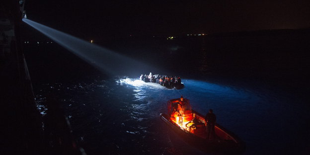 Zwei Boote nachts auf dem Wasser, eins wird angeleuchtet