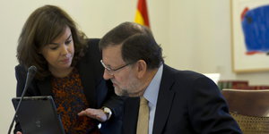 ein Mann und eine Frau mit Tablet-Computer und Mikrofon, hinter ihnen eine Spanien-Fahne