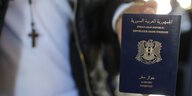 Mensch mit Kette mit Kreuz um den Hals im Hintergrund zeigt seinen syrischen Pass im Vordergrund