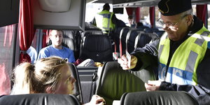 Ein Polizist kontrolliert einen Ausweis einer jungen Frau in einem Bus