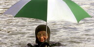 Ein Mensch im Taucheranzug schimmt im Wasser und hält einen grün-weißen Regenschirm über sich