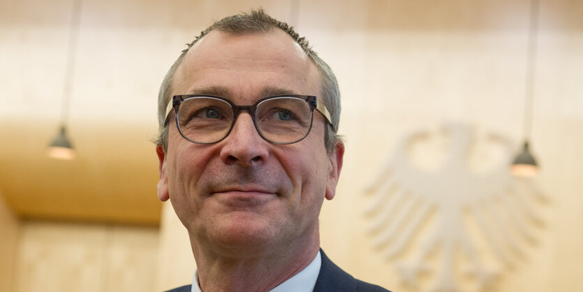 Volker Beck steht lächelnd vor einem Bundesadler