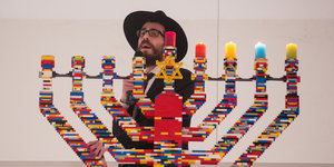 Ein Rabbi steht singend hinter einem Chanukka-Leuchter aus Legosteinen