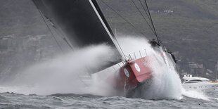 Segelschiff liegt schräg im Wasser, Gischt spritzt über das Boot