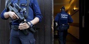 Ein Polizsit mit Sturmgewehr, man sieht sein Gesicht nicht, ein anderer Polizist geht in ein Gebäude