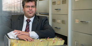 Mann stützt sich auf Schublade mit Karteikarten, neben ihm eine Karteikastenwand