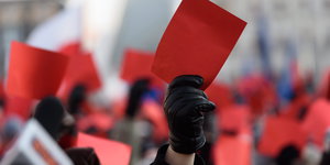 Menschen mit schwarzen Handschuhen halten rote Karten in die Luft