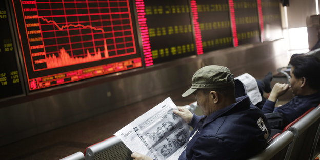 Zwei Männer lesen Zeitung vor einer roten Anzeige mit Aktienkursen