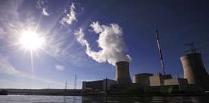 Atomkraftwerk mit dampfendem Kühlturm unter einem blauen Himmel.
