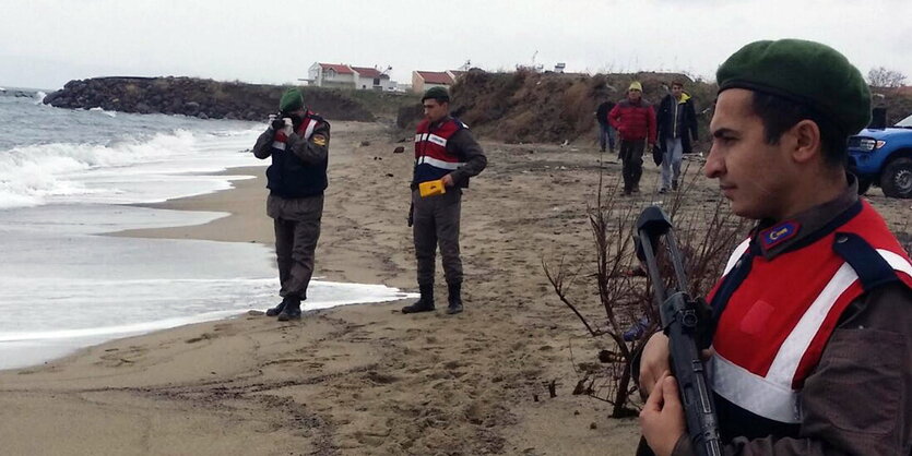 Drei Männer in Uniformen stehen am Strand