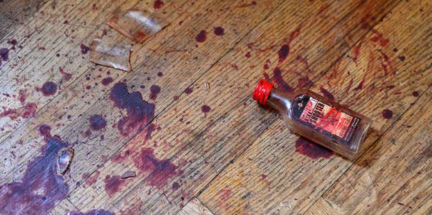 Eine Flasche liegt auf einem blutverschmierten Boden
