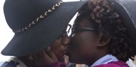 Zwei Frauen mit Brillen und Hüten küssen sich