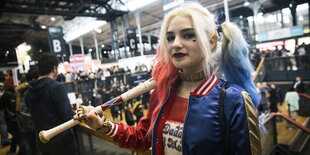 Ein Frau mit blau-rot-weißen Haaren hält einen Baseballschläger in der Hand