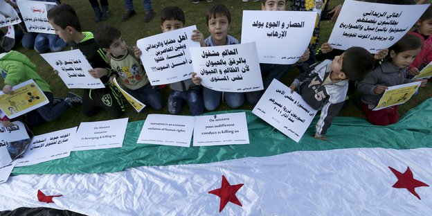 Kinder mit Plakaten über einer syrischen Flagge