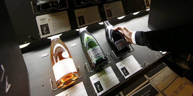 Eine Person zeigt auf eine Champagner-Flasche im Regal eines Weinladens.