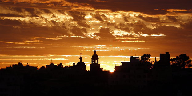 Die schwarze Siluette von Hebron, dahinter gold-braunes Licht der untergehenden Sonne