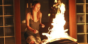 Eine junge Frau sitzt in einer Wohnung vor einem Feuer