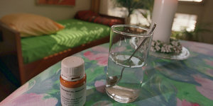 Ein Fläschchen mit einem Betäubungsmittel und ein Glas Wasser stehen in einem Zimmer auf einem Tisch.