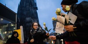 Ein Tunesier gibt einer Frau eine weiße Rose, dahinter der Kölner Dom