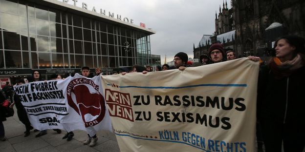 Demonstranten vor dem Kölner Bahnhof halten ein Banner hoch