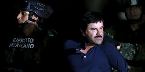 Drogenboss Joaquín „El Chapo“ Guzmán, in einem blauen T-Shirt, eskortiert von zwei Polizisten