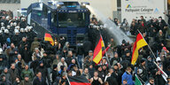 Eine Menschenmenge, im Hintergrund ein Wasserwerfer der Polizei, der im Einsatz ist