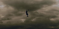 Eine Person fährt mit einer Seilbahn vor bewölktem Himmel