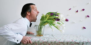 Ein Mann schreit eine Vase an, in der sich die Tulpen biegen