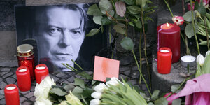 Blumen, Kerzen und Karten für David Bowie liegen am neben einen Foto des Musikers