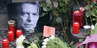 Blumen, Kerzen und Karten für David Bowie liegen am neben einen Foto des Musikers