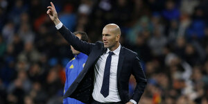 Zinédine Zidane steht am Spielfeldrand und hebt seinen Arm in Richtung eines vorbeifliegenden Balles