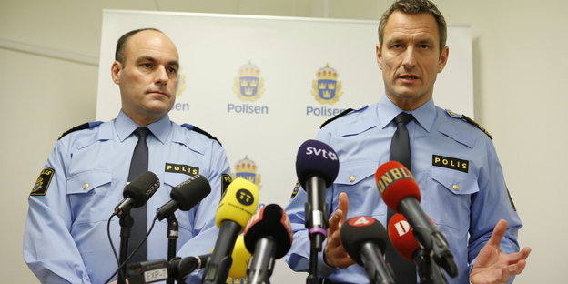 Zwei schweidische Polizisten stehen vor vielen Mikrofonen