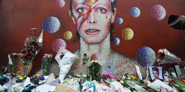Blumen und Karten liegen vor einem Kunstwerk, das David Bowie zeigt