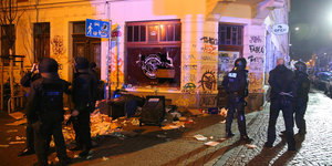 Polizisten stehen am 11.01.2016 im Stadtteil Connewitz in Leipzig vor zerbrochenen Fensterscheiben und verwüsteten Müllcontainern.