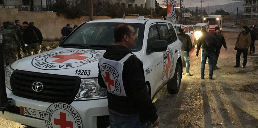 Ein Auto steht auf einer Straße für Madaja, darum herum stehen Menschen