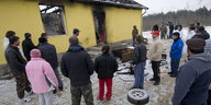 Menschen stehen vor einem ausgebrannten Haus.