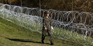Soldat läuft an Zaun aus Stacheldrahtrollen entlang