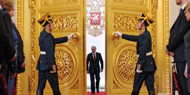 Wladimir Putin schreitet durch eine riesige goldene Flügeltür, die von zwei Uniformierten geöffnet wird