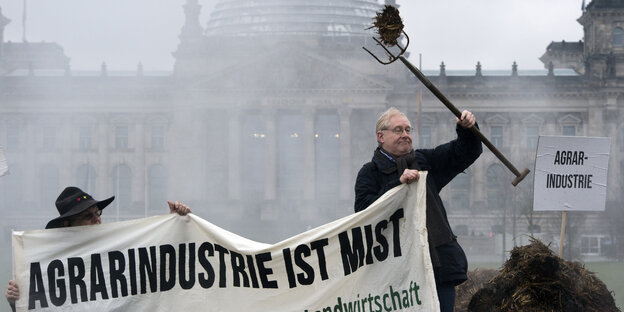 Ein Mann mit einer Mistgabel hält ein Transparent mit dem Aufdruck "Agrarindustrie ist Mist"