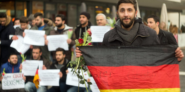 Ein Mann mit Deutschlandflagge vor weiteren Männern mit Blumen